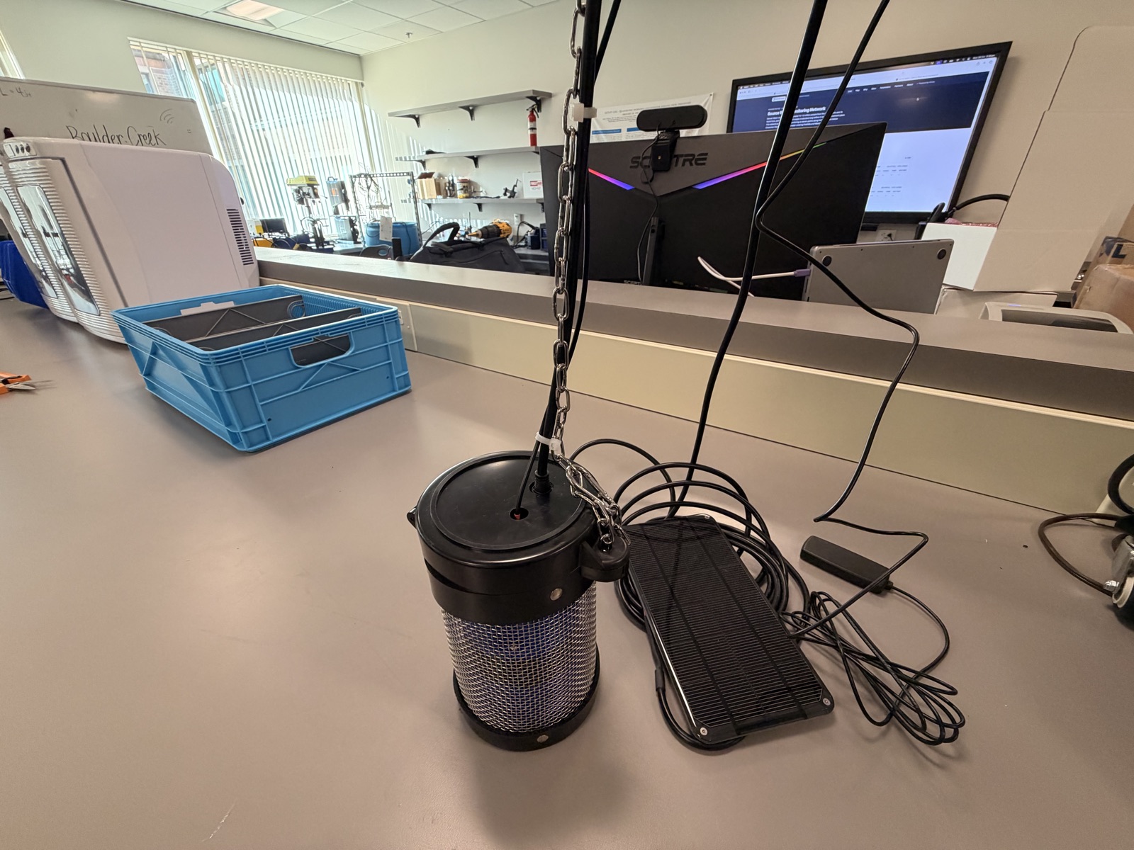Assembled enclosure hanging from its chain with solar panel and antenna on their leads